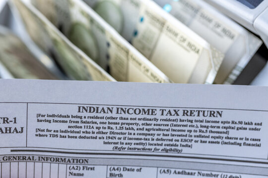 Indian income tax return form and rupees banknotes inside counting machine. Economic concept of India taxation system, government revenue, fiscal policy and corporate accounting.