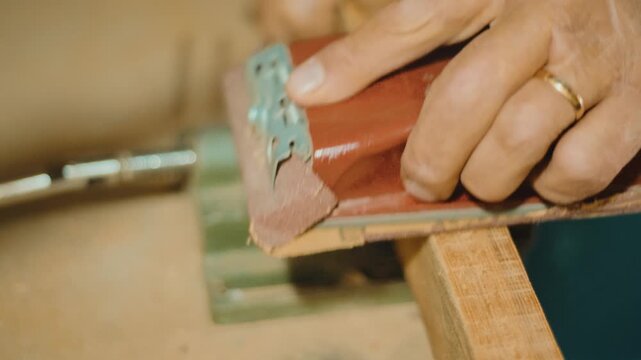 Macro shot of skilled hands using a sanding block to smooth a wooden surface. Focus on texture, precision and craftsmanship for woodworking and DIY content
