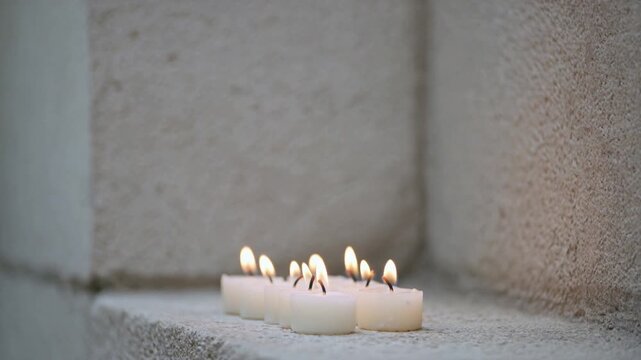 Row of small lit candles in a stone alcove close up