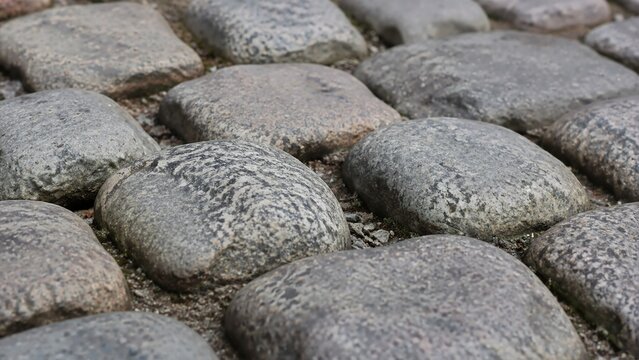 Rounded granite cobblestone street pavement in close-up. Historic road surface paved with rough stone blocks