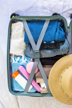 Open suitcase filled with neatly packed clothing, sunglasses, sunscreen, and a straw hat, ready for a summer vacation or beach getaway