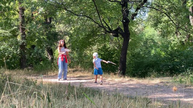 A loving mother and her joyful young son play badminton together. The excited boy holds his racket on a dirt path in a sunny park. They enjoy a happy summer day.