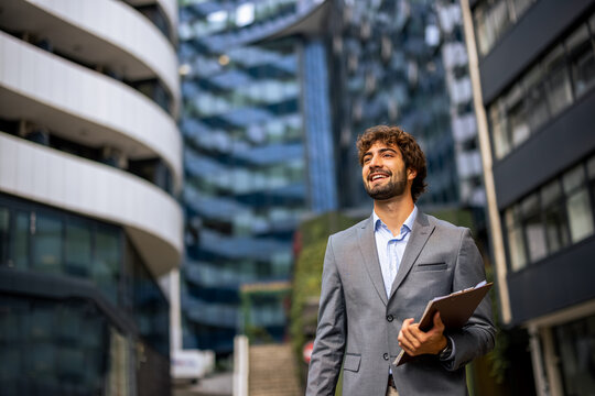 Young businessman walking in city center with folder, corporate ambition and leadership in modern urban environment