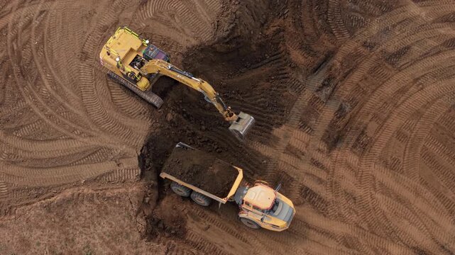 Top down aerial view of an excavator loading excavated soil into a heavy dump truck on a construction site in the UK