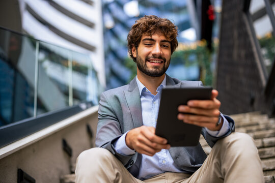 Smiling businessman holding tablet while sitting on outdoor office stairs