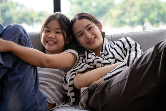 Two teenage girls smiling together on sofa at home, showing friendship, happiness, bonding, relaxed lifestyle, cheerful companionship and comfortable indoor leisure