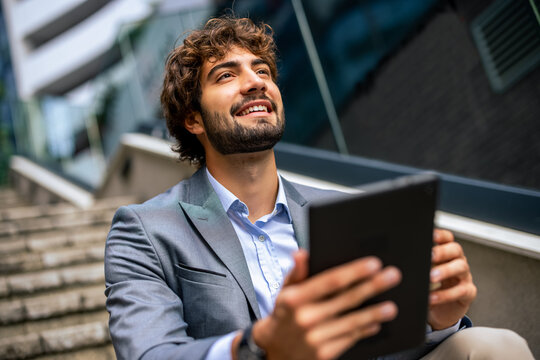 Low angle close up of smiling businessman holding tablet looking away