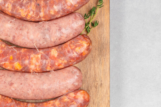 Assorted cured sausages arranged on wooden board with herbs and spacious light background for culinary presentation, overhead food still life composition