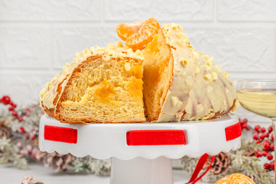 Sliced holiday bundt cake with creamy glaze, almond topping, orange garnish, and red ribbon on white cake stand against textured brick background