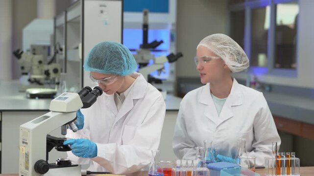 Two female scientists conducting chemical experiments and microscopy in a modern laboratory setting