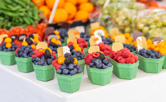 Colorful fresh berry baskets with blueberries raspberries and blackberries arranged at an outdoor market alongside other produce in a vibrant farm stand display