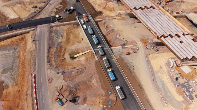 Aerial view of tipper trucks lined up in a queue waiting to deliver asphalt at a highway construction site in Bedfordshire, UK