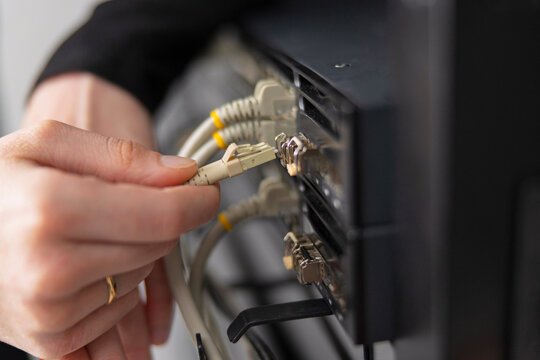 Adult IT technician maintains data center by connecting network cables to a server rack for troubleshooting and updates