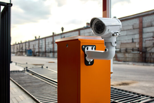 White dome security camera mounted on orange access control post overlooking industrial loading dock area at dusk under overcast cloudy sky