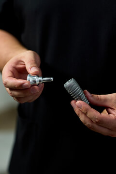 Closeup of hands threading metal hose connector fittings together, assembling garden plumbing hardware under neutral indoor lighting with sharp focus on textured threads