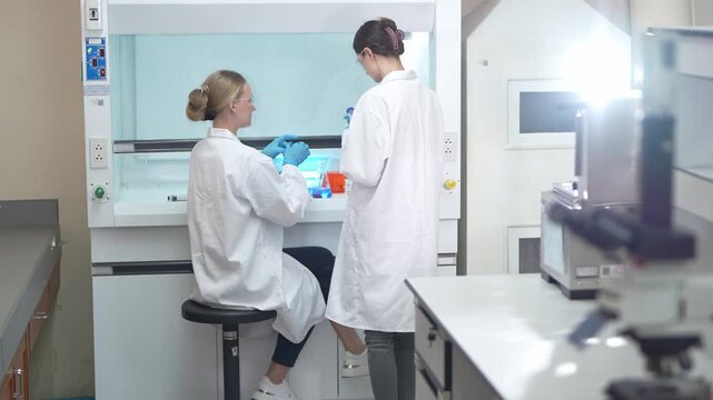 Two female scientists conducting chemical experiments inside a laboratory fume hood environment