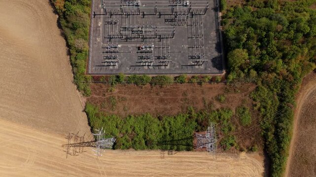 Top down aerial view of an electrical transmission substation connecting to high voltage pylon lines in Eaton Socon, UK