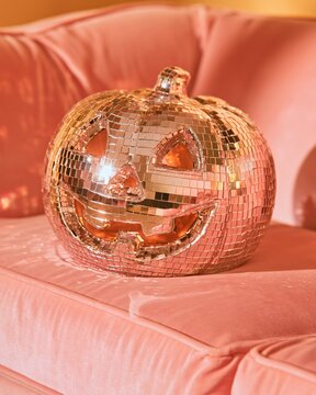 A disco ball pumpkin sits on a pink couch, adding to the Halloween vibe