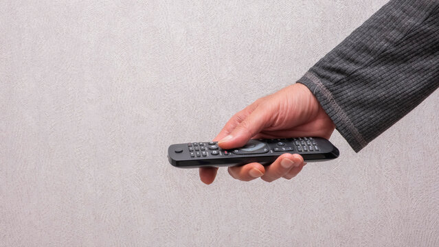 Hand holding a black television remote control. This image is perfect for technology, entertainment, home leisure, and lifestyle media projects.