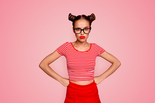 Strict teacher! Portrait of grimacing offended young gorgeous woman model with with hands on waist and bun hairstyle isolated on red background