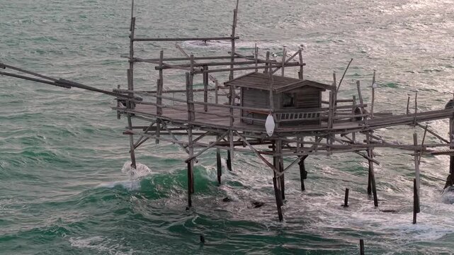 Trabocco Turchino lonely wooden pier aerial 70mm drone view in Abruzzo Italy. Cinematic slow flyby of historic stilt pavilion with crashing waves 4K