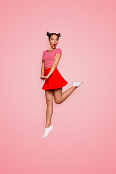 Full-length full-size vertical view of jumping and wondered brunette woman dressed in colourful bright clothes isolated on red background