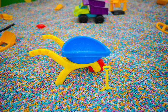 Various colorful plastic toys and shovels scattered in a sensory pit filled with multi colored foam beads at an indoor kids playground.