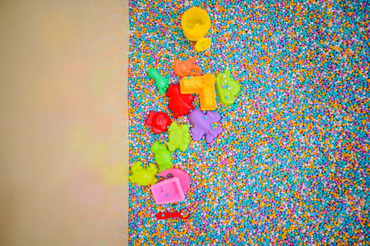 Various colorful plastic toys and shovels scattered in a sensory pit filled with multi colored foam beads at an indoor kids playground.