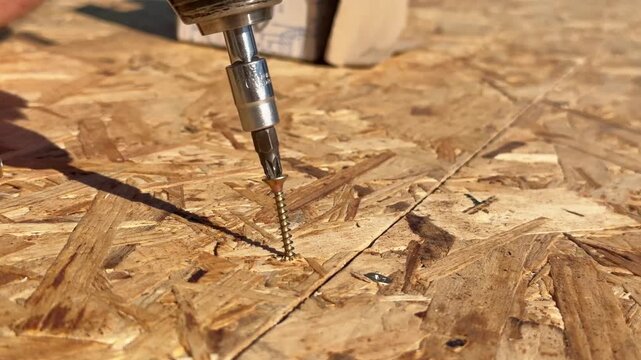Close up of screws being driven into OSB board with a power drill, DIY renovation, skilled craftsmanship