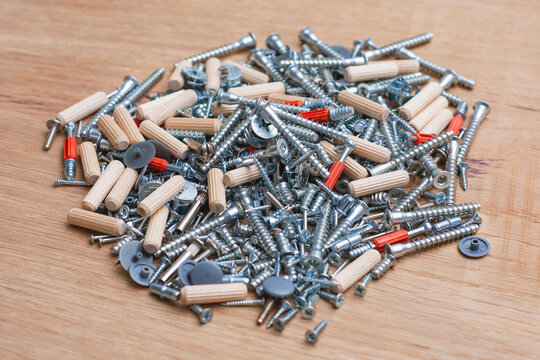 Pile of mixed furniture assembly hardware with screws, dowels and fasteners on wooden surface. Hardware store and furniture manufacturing guides.