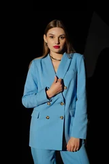 Beautiful fashionable woman wearing trendy blue color suit blazer, pants, stylish necklace, posing on black background. Waist up studio fashion portrait © Victoria Fox