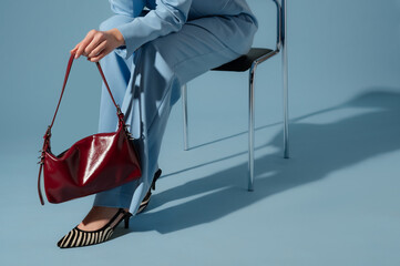 Close up photo of trendy burgundy red faux leather bag, purse in elegant outfit. Woman wearing blue suit, zebra print shoes. Spring, summer fashion details. Copy, empty, blank space for text