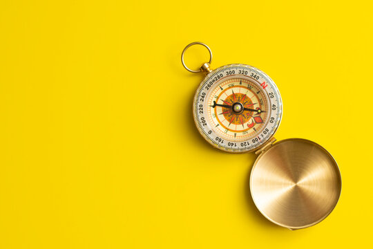 Vintage brass pocket compass open on bright yellow background with copy space. Business navigation, strategic direction, career path guidance, decision making and strategic leadership concept.