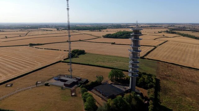 Detailed aerial view of steel transmission tower spire and radio frequency broadcast gear above parched English countryside