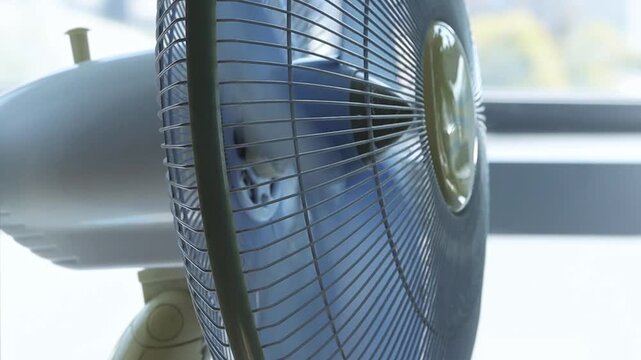 Fan spinning close up. Cooling air circulation from a spinning white electric fan placed near a bright window during the day to help stay comfortable in the warm indoor space
