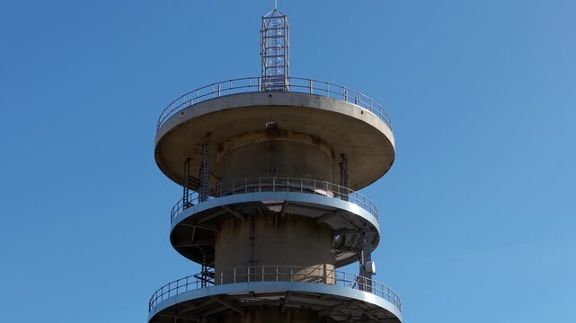 Close-up aerial view of the pinnacle and antenna array of a telecommunications transmitter mast over dry summer fields in the UK