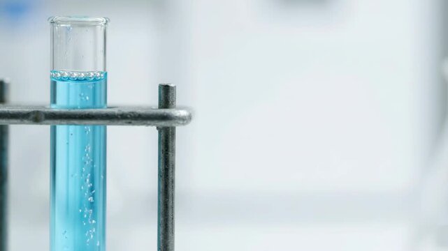 Bubbles rising in a test tube filled with blue liquid. Close-up of a chemical reaction in a laboratory setting. Scientific research and experiment concept