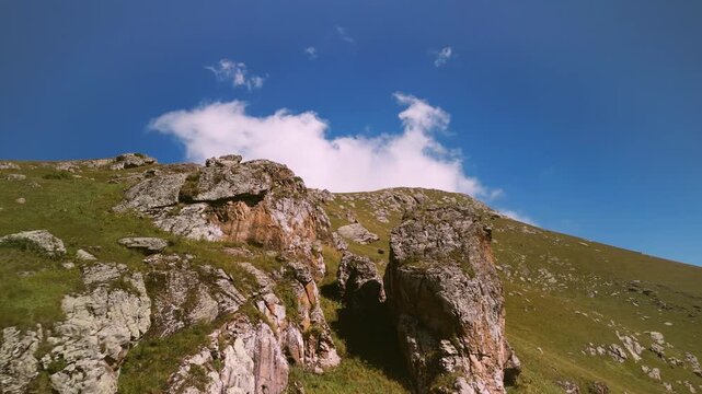Aerial Drone Flight Along Rugged Rock Formations on a Green Mountain Ridge Under Blue Sky with White Cloud in Armenia