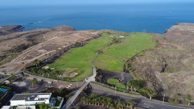 Vuelo a&eacute;reo sobre calles de golf verdes y b&uacute;nkeres entre colinas volc&aacute;nicas con el oc&eacute;ano azul delante, Adeje, Tenerife
