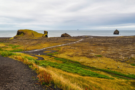Coastline of the Atlantic Ocean. Black pebble trail, green fields, basalt rocks of Reykjanest&aacute; or Valahn&uacute;kam&ouml;l. Famous Valahn&uacute;kur coast and Karlinn (&bdquo;The Man&ldquo;) sea cliff, Reykjanes Peninsula, Iceland.