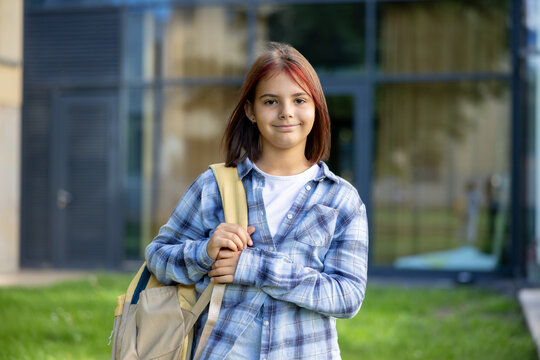 Young student girl carrying backpack outside school building