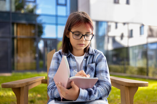 Young girl student writing in notebook outdoors learning