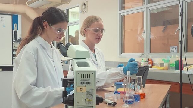 Two female scientists conducting research with a microscope in a modern laboratory environment