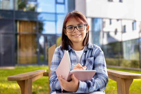 Young student girl writing in notebook outdoors on campus
