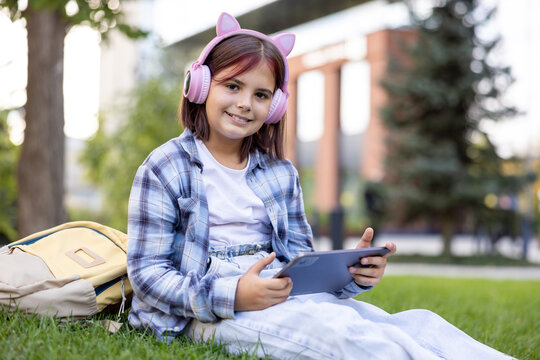 Schoolgirl with headphones using tablet learning outdoors on grass