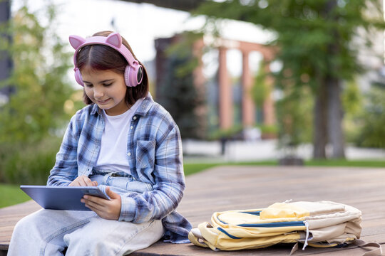 Young girl wearing headphones learning outdoors using tablet