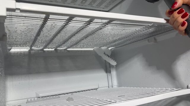 Defrosting a freezer with a hair dryer, warm air melting ice, water dripping, chunks falling, a candid authentic life chore moment at home today very real and cold, right now.