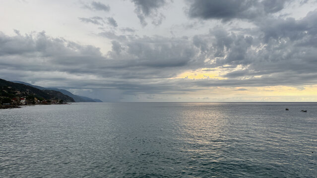 Spectacular cloudy sky over calm ocean waters at sunset with a mountainous coastline