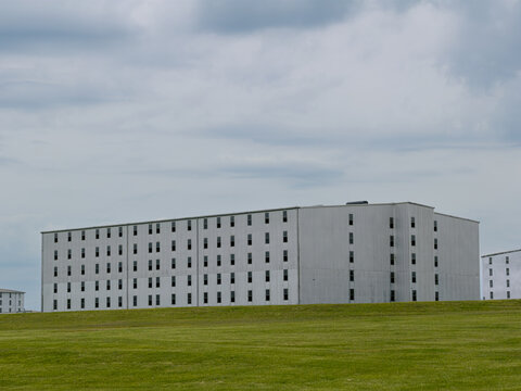 Large, multi-story white rick house, where bourbon is aged in oak barrels, with rows of small windows stands above a mowed green lawn under a soft gray, cloudy sky, Bardstown, Kentucky