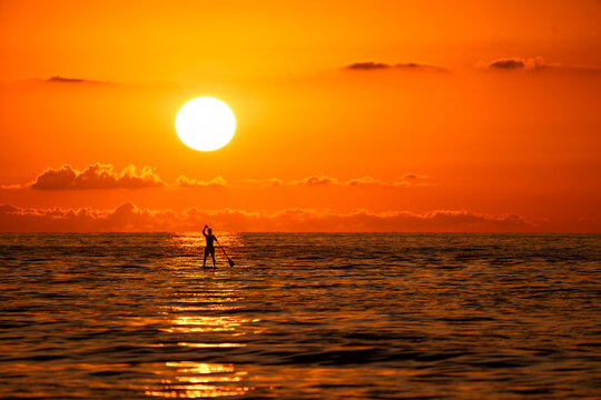 A man paddleboarding at sunset